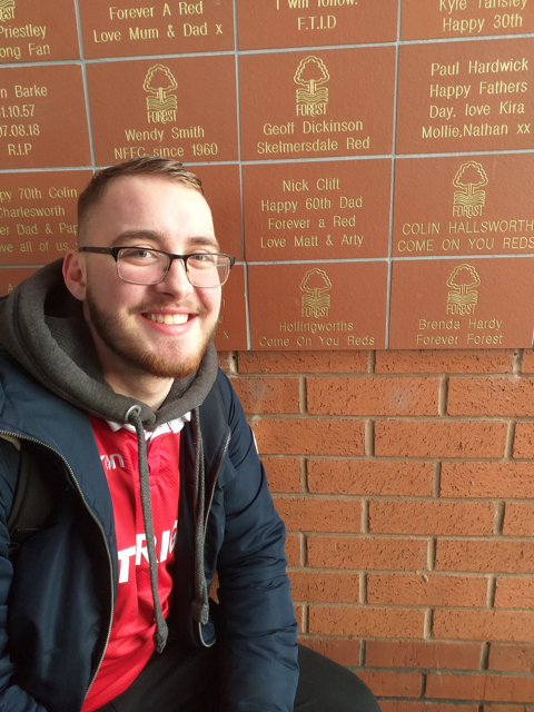 Matthew posing in front of the supporter's wall at the Nottingham Football Club.